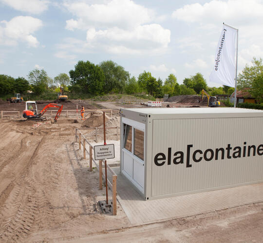 Außenansicht einzelner Baucontainer auf Baustelle mit Logo von ELA Container