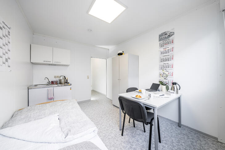 Innenansicht Wohncontainer mit Bett, Küche und Schreibtisch sowie einem Schrank