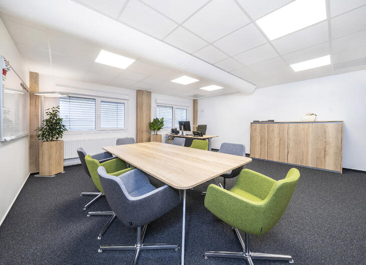 Besprechungsraum mit Filzboden, Tisch, Stühlen und Schreibtisch