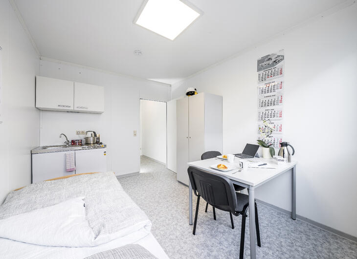 Innenansicht Wohncontainer mit Bett, Küche und Schreibtisch sowie einem Schrank