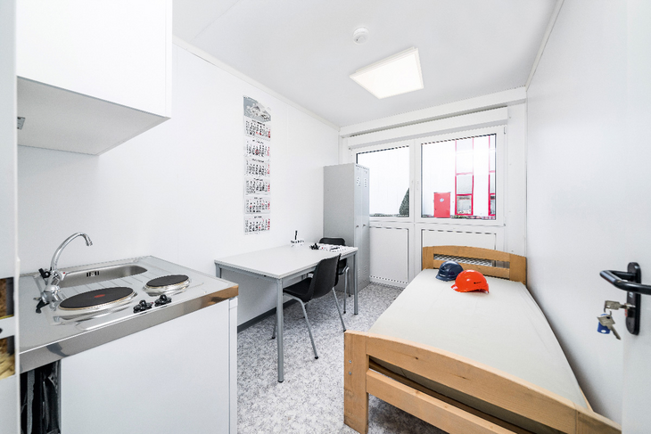 Wohncontainer Innenansicht mit Waschbecken, Bett und Schreibtisch