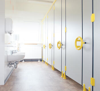 Sanitetsmodul til børnehave med gule håndtag på dørene til toiletbåsene.