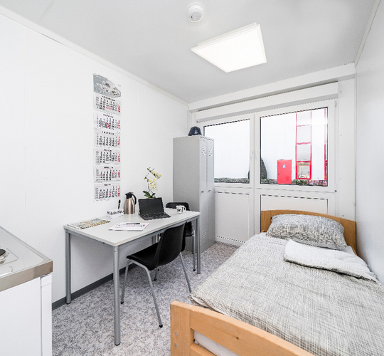 Boligmodul med seng, tekøkken, bord, stole og skabe