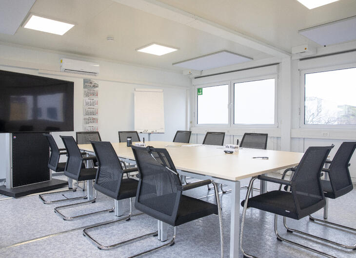 Mødelokale med bord, stole og tv-skærm