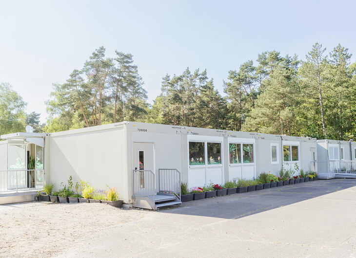 Mellemstor skolebygning med flere indgange og blomsterkrukker omkring