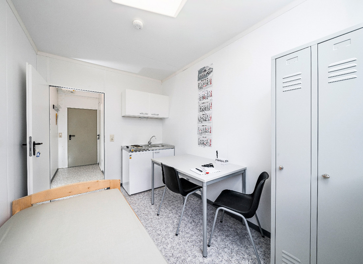 Værelse i modulby med seng, skabe, tekøkken og bord