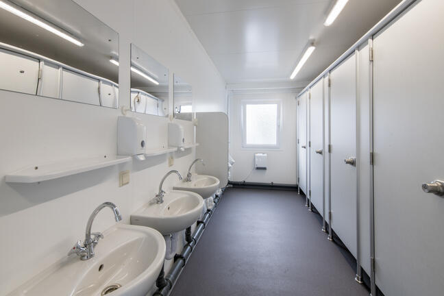 Indvendigt i en toiletcontainer med toiletkabiner og håndvaske