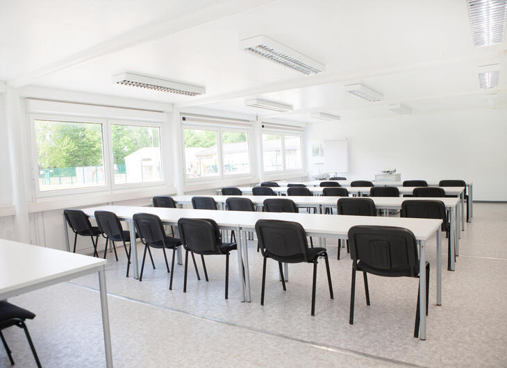 Innenansicht Klassenzimmer Schulcontainer mit weißen Tischen und schwarzen Stühlen - ELA Container