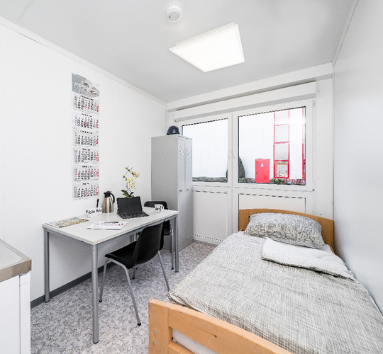 Bostadsmodul med säng, pentry, bord, stolar och skåp