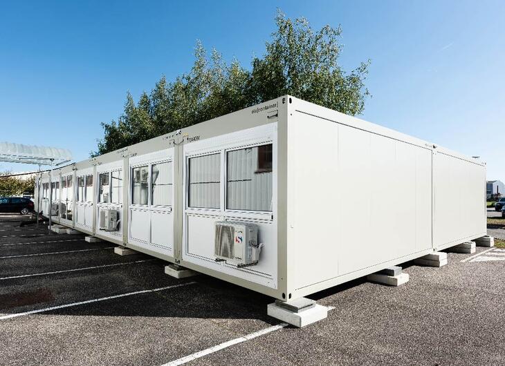 Ljusgrå mellanstor kontorsanläggning på en parkeringsplats