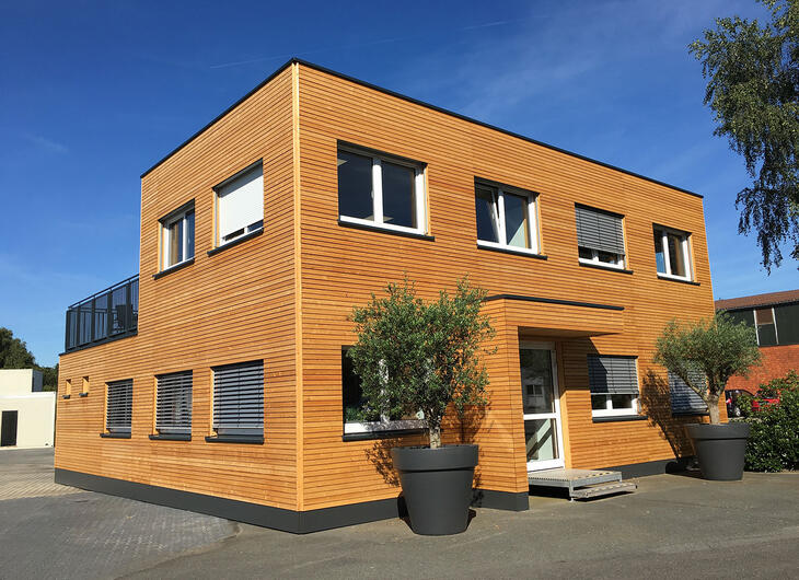 Större containerbyggnad, träklädd med takterrass och metallräcke